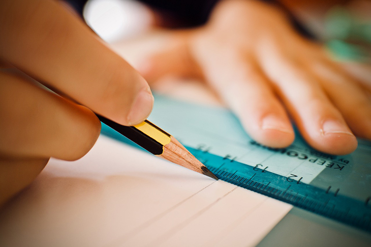En närbild på ett par händer som drar ett streck med hjälp av en linjal.